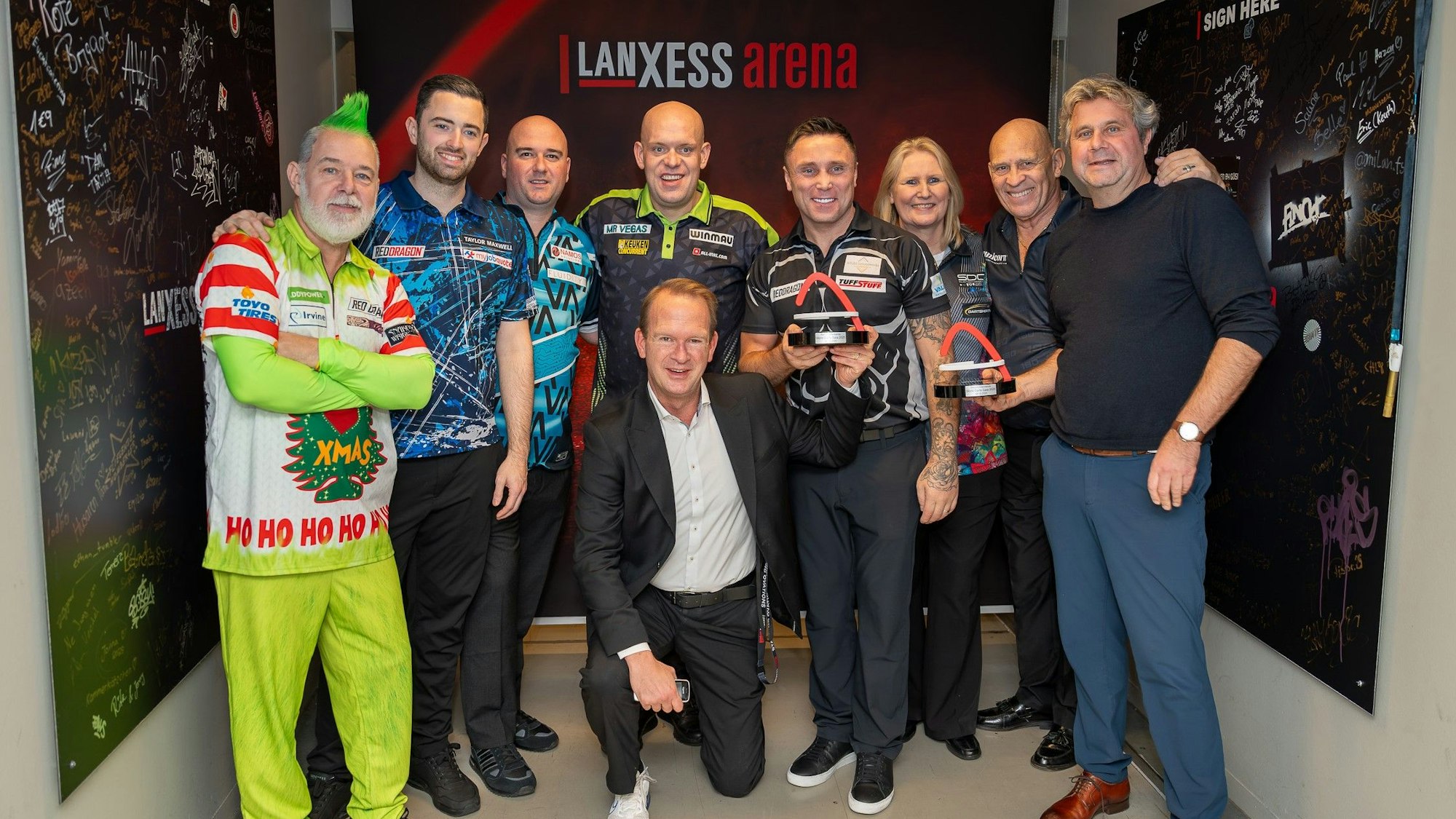 Die teilnehmenden Dartsspielerinnen und Dartsspieler posieren mit Veranstalter und Arena-Geschäftsführer für ein gemeinsames Foto.