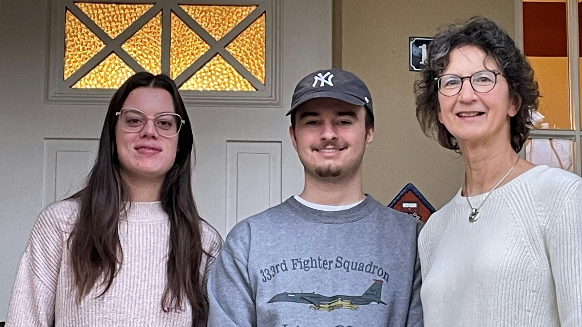 Zwei Studenten und eine ältere Frau lächeln in die Kamera.