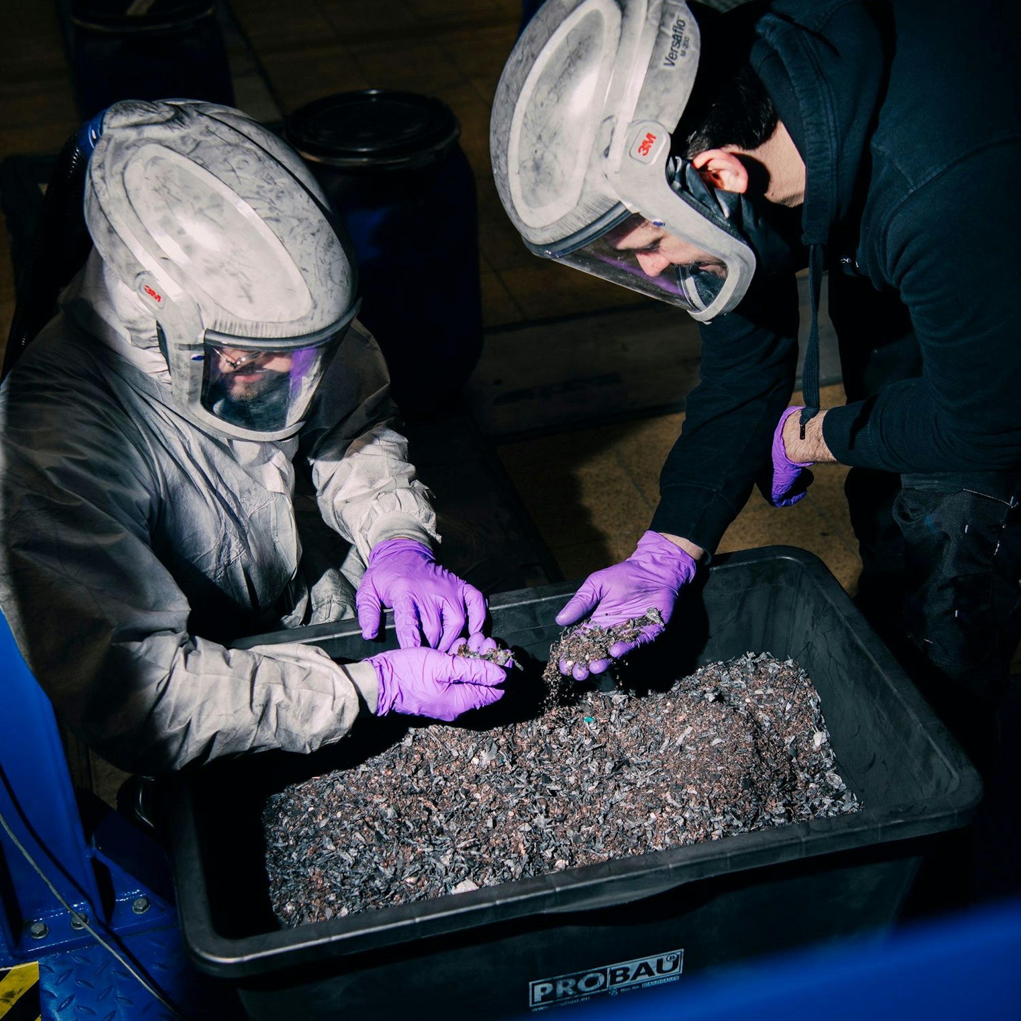 Zwei Männer in Schutzkleidung beugen sich über eine Plastikwanne mit Schwarzmasse.