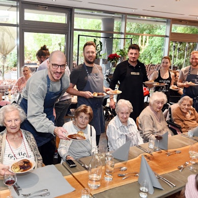 12.08.2025 Köln. Die gute Tat: Benefizaktion Gänseessen für Senioren der Diakonie Michaelshoven im Neobiota. Erik Scheffler (weißes T-Shirt) und Freunde servieren den Senieren das Essen. Foto: Alexander Schwaiger