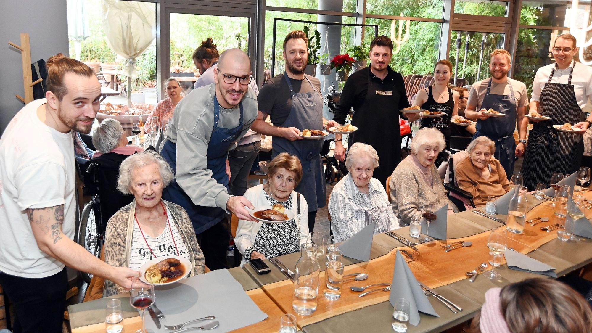 12.08.2025 Köln. Die gute Tat: Benefizaktion Gänseessen für Senioren der Diakonie Michaelshoven im Neobiota. Erik Scheffler (weißes T-Shirt) und Freunde servieren den Senieren das Essen. Foto: Alexander Schwaiger