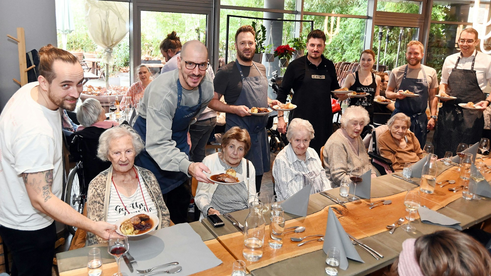 12.08.2025 Köln. Die gute Tat: Benefizaktion Gänseessen für Senioren der Diakonie Michaelshoven im Neobiota. Erik Scheffler (weißes T-Shirt) und Freunde servieren den Senieren das Essen. Foto: Alexander Schwaiger