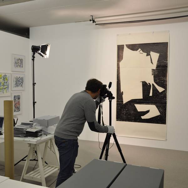 Ein Mann fotografiert ein Kunstwerk, es hängt an einer Wand.