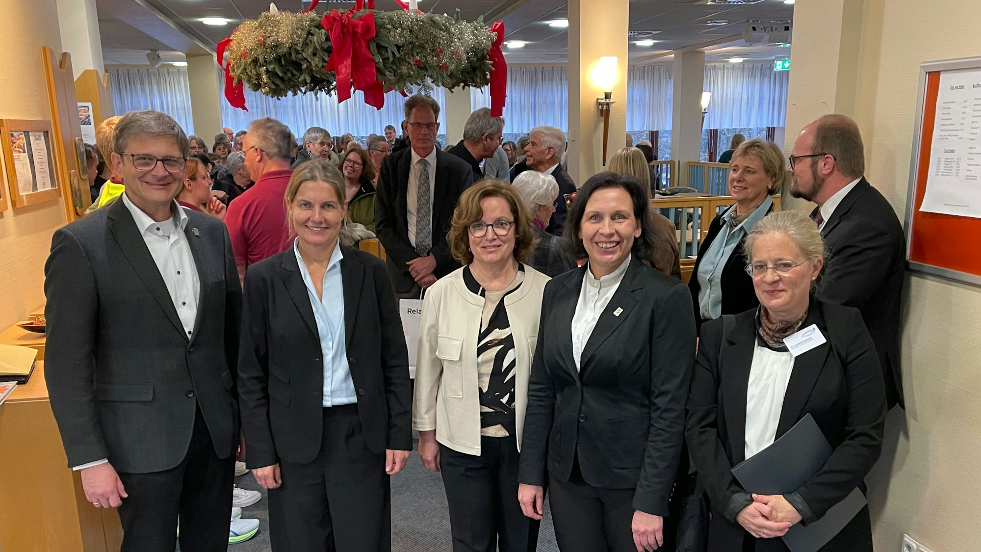 Der Mann und die vier Frauen stehen in einer Reihe am Eingang der Cafeteria, in der sich weitere Gäste versammelt haben.
