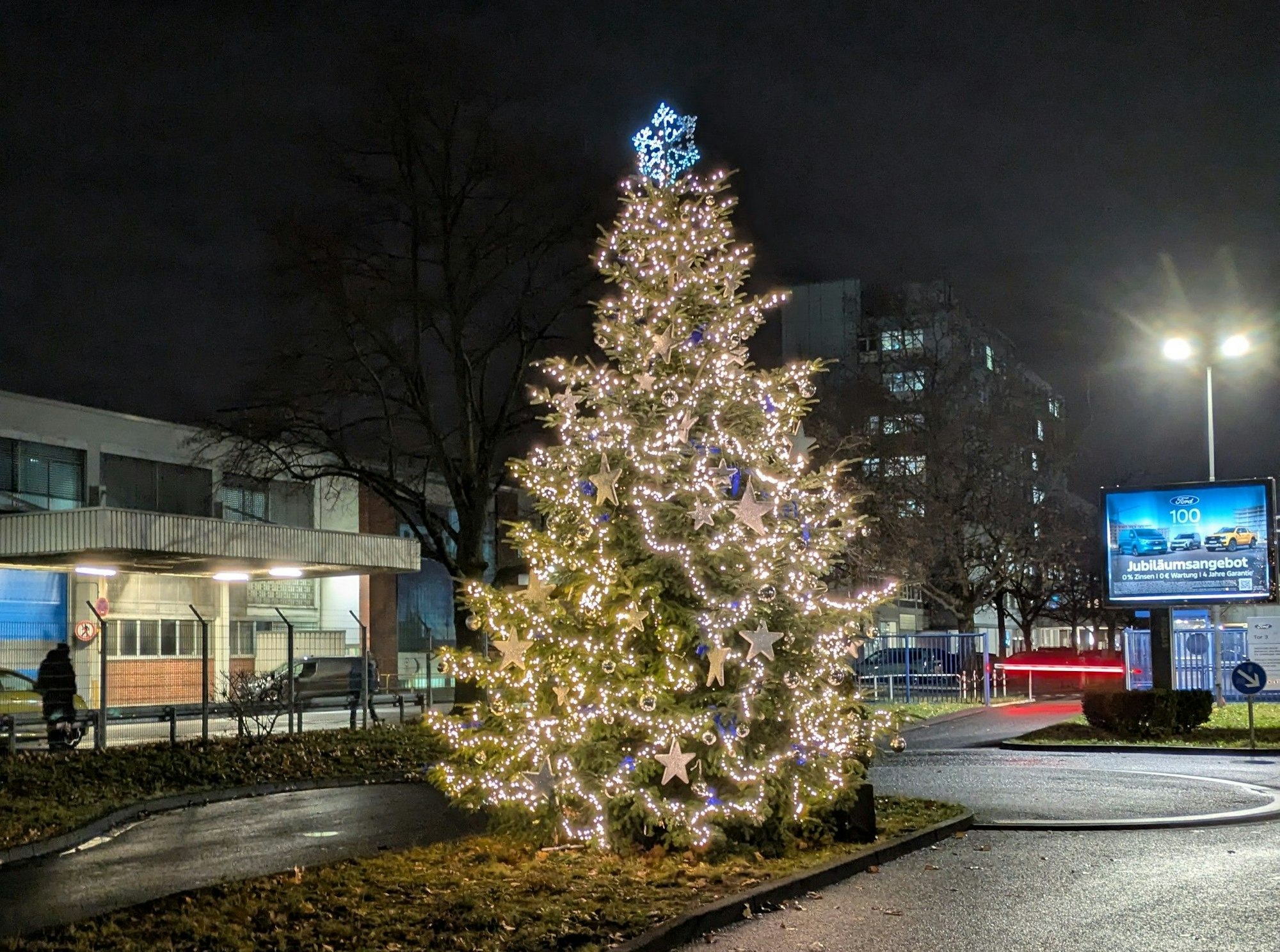 Weihnachtsbaum mit Lichterketten strahlt in der Dunkelheit.