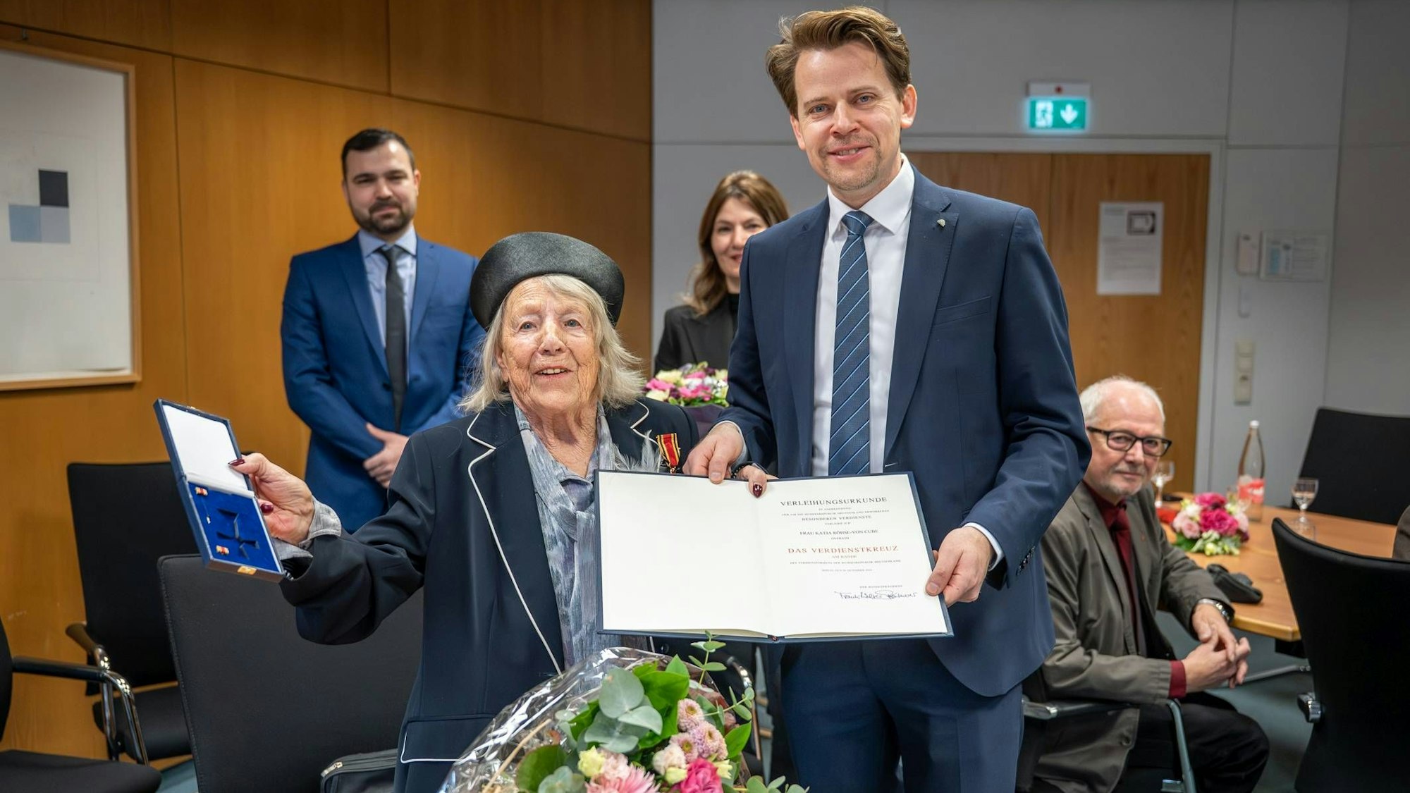 Eine ältere Dame und ein jüngerer Mann schauen in die Kamera und lächeln.