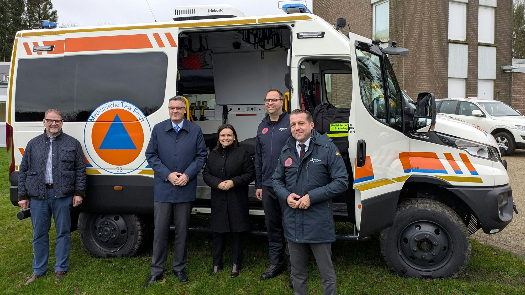 Vier Männer und eine Frau stehen vor einem Mannschaftstransportwagen der Medizinischen Task Force.