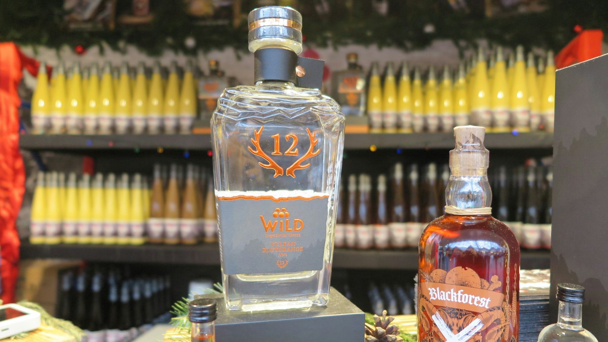 Das Bild zeigt eine Flasche des Brandes „Blutorangengeist“; im Hintergrund befinden sich Liköre.