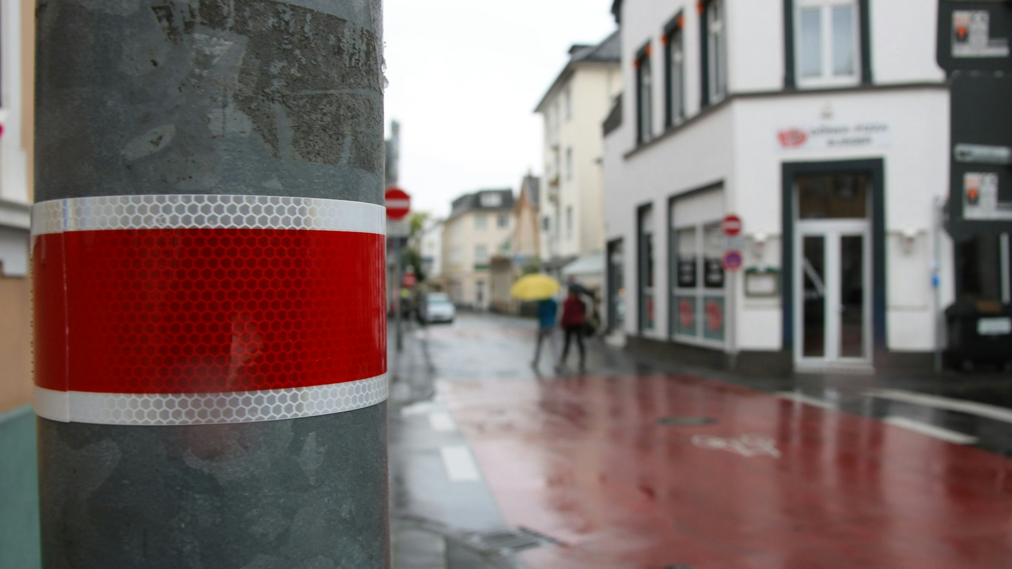 Ein roter Streifen an einem Lampenmast, der an einer rot markierten Fahrradstraße steht.
