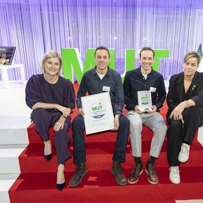 Das Foto zeigt die Preisträger auf einer Treppe mit rotem Teppich sitzend mit den Urkunden in der Hand.