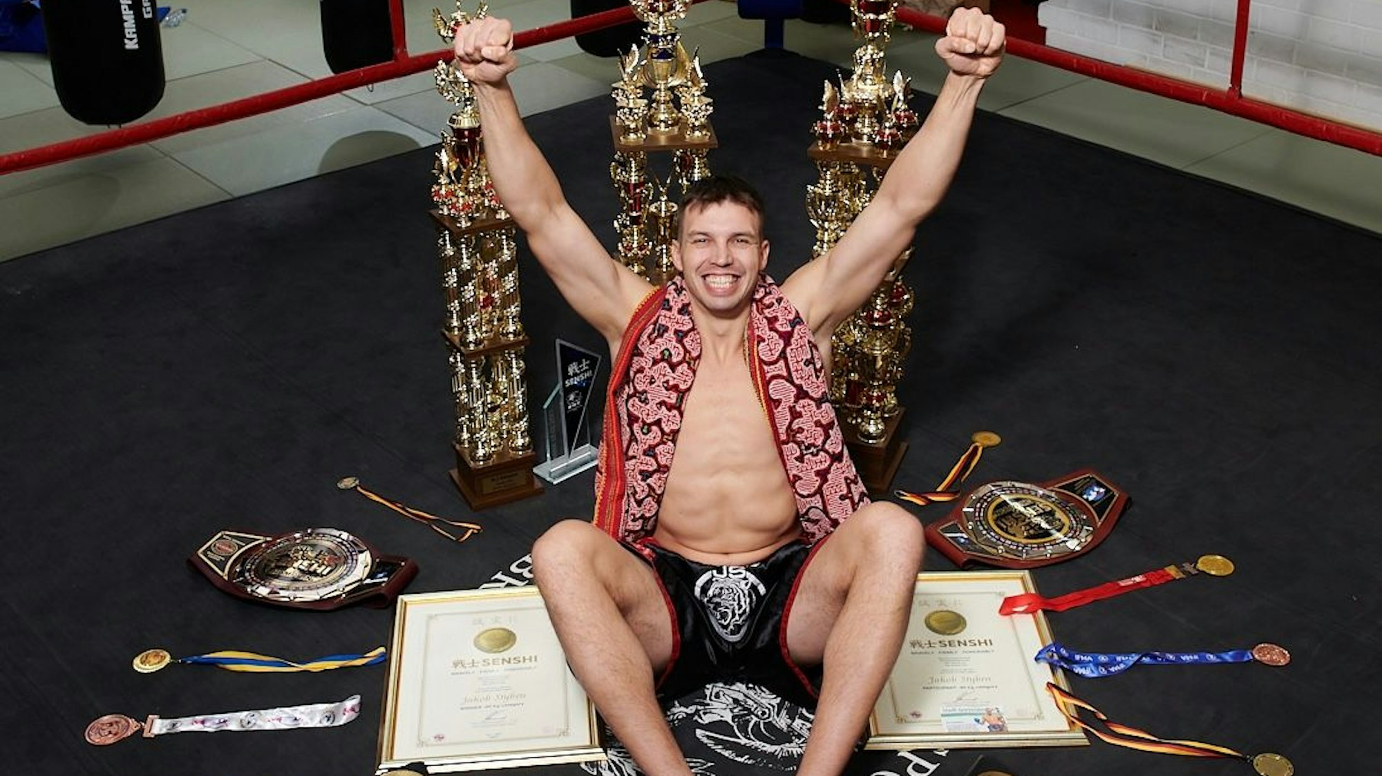 Jakob Styben ist Profi-Kickboxer, mehrfacher Deutscher Meister und international erfolgreicher Medaillengewinner. Er sitzt auf dem Boden, umgeben von etlichen Medaillen und Urkunden