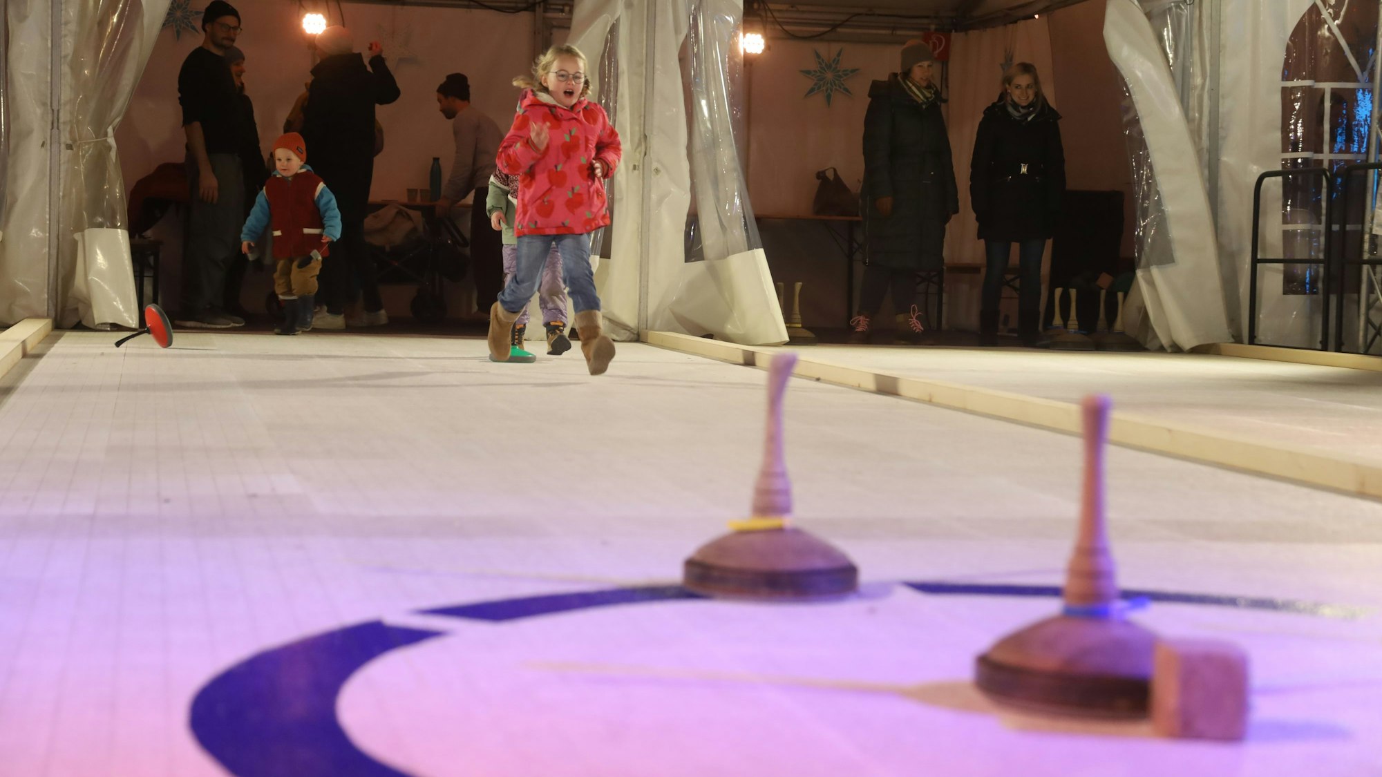 Besucher auf der Eisstockbahn auf dem Ebertplatz. Ein Mädchen läuft über die Bahn.
