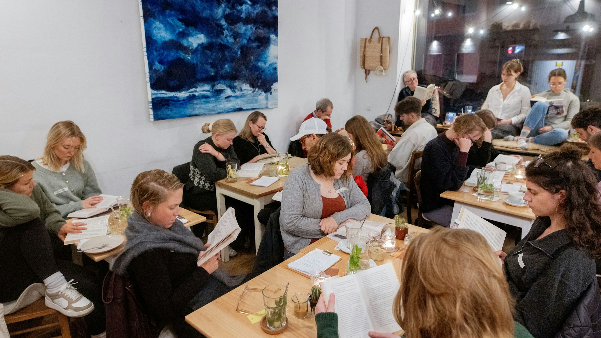 Menschen lesen gemeinsam bei der „Horizonte Leseparty“ im Café Mexi in Köln-Nippes.