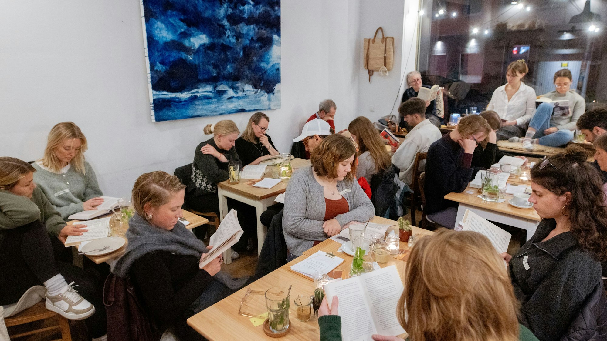 Menschen lesen gemeinsam bei der „Horizonte Leseparty“ im Café Mexi in Köln-Nippes.