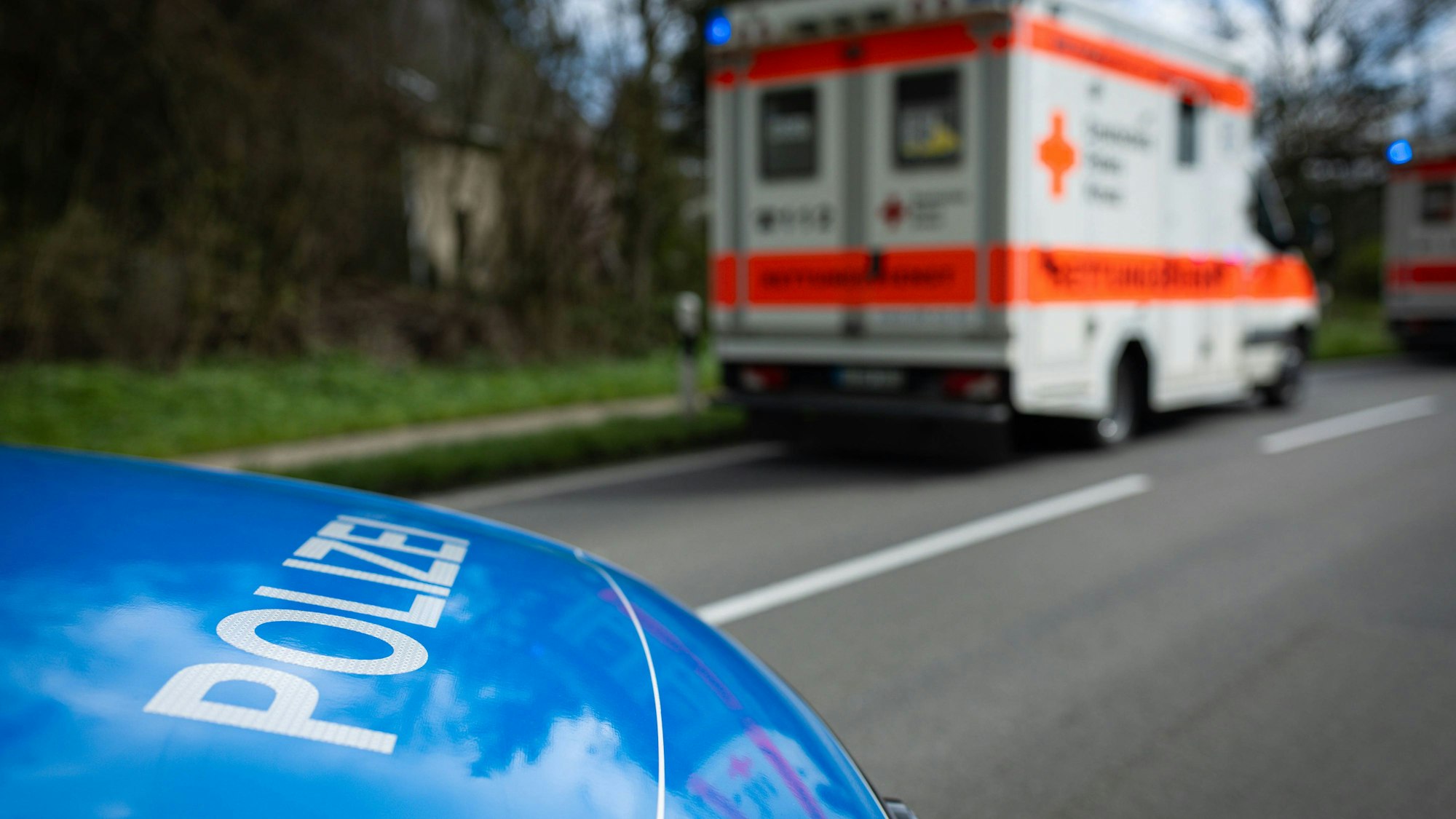 Ein Krankenwagen mit Blaulicht und ein Polizeiauto stehen auf einer Straße.