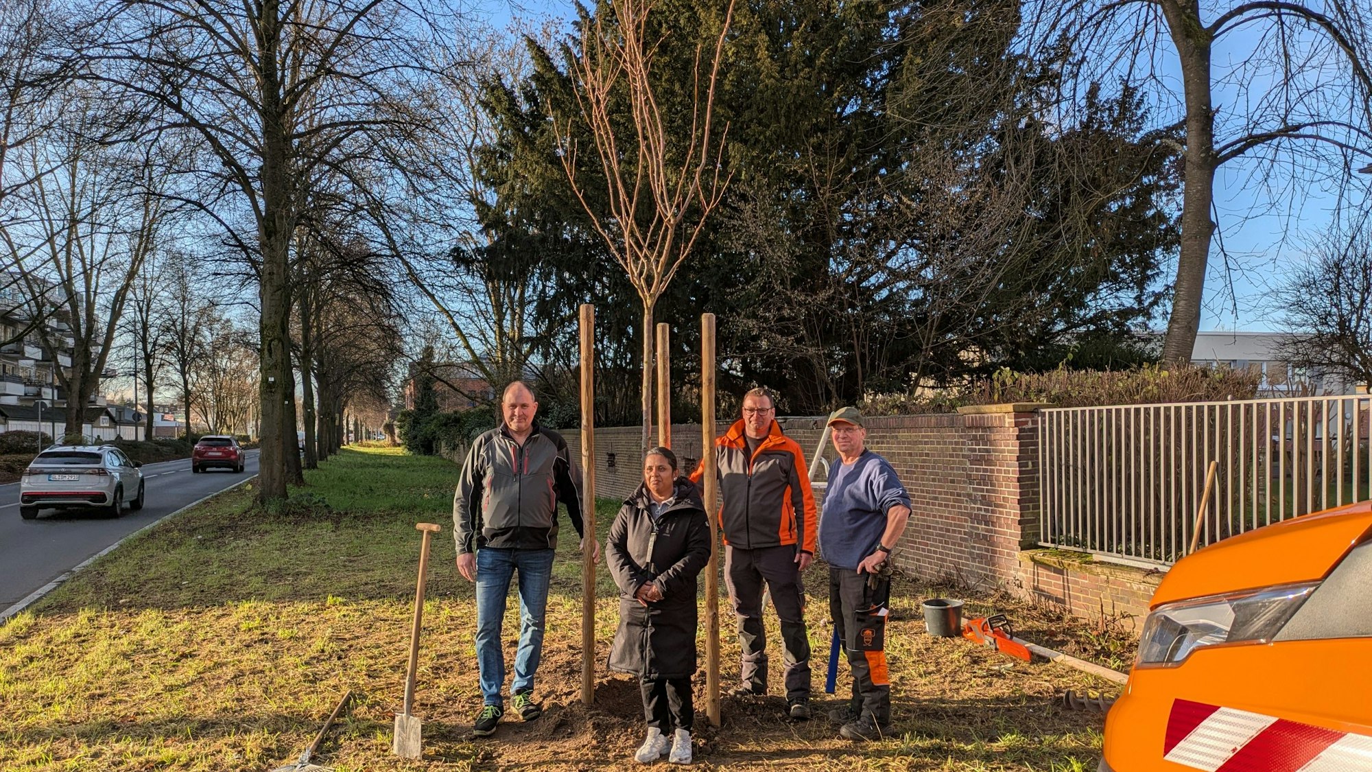 Drei Männer und eine Frau stehen vor einem frisch gepflanzten Baum.