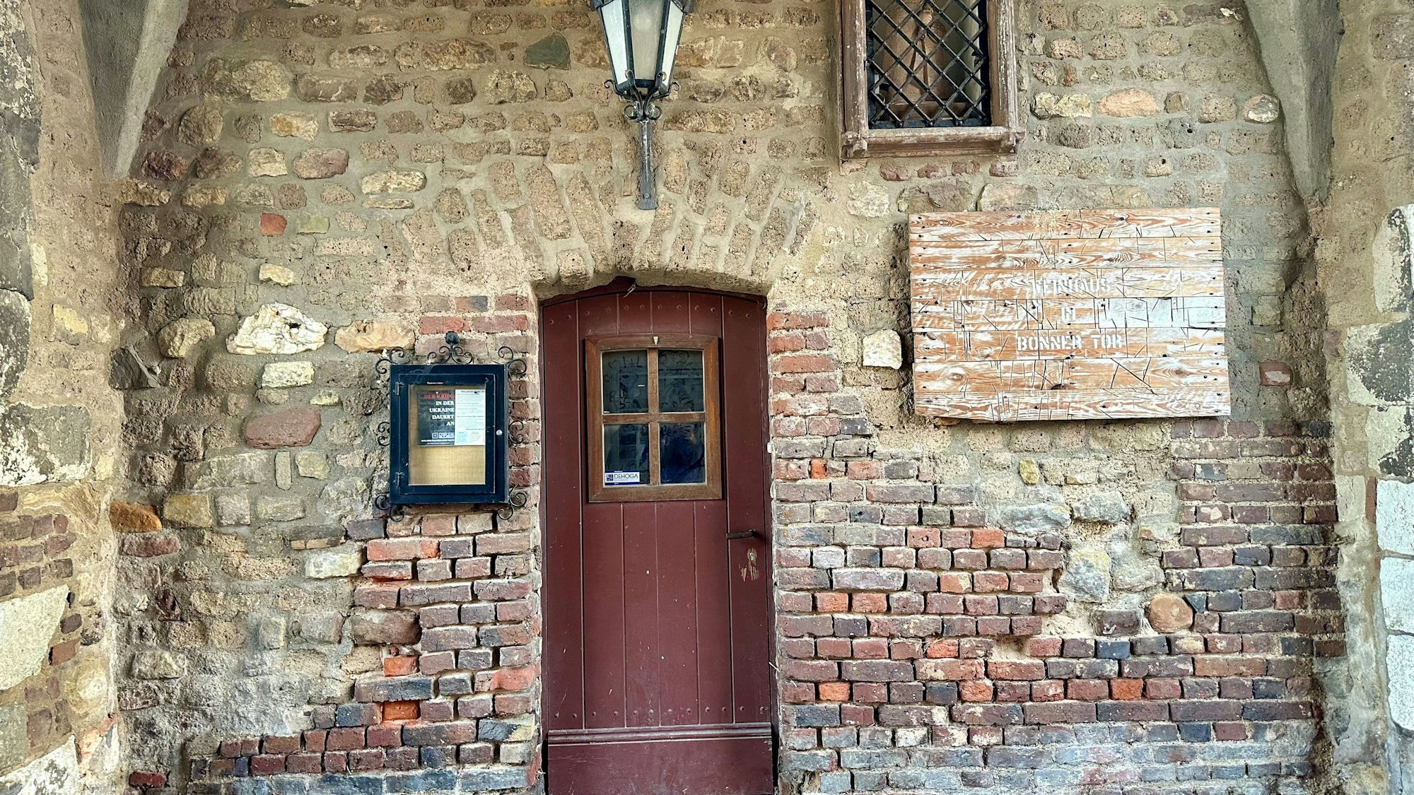 Zu sehen ist eine Holztür in einem Backstein-Gebäude.