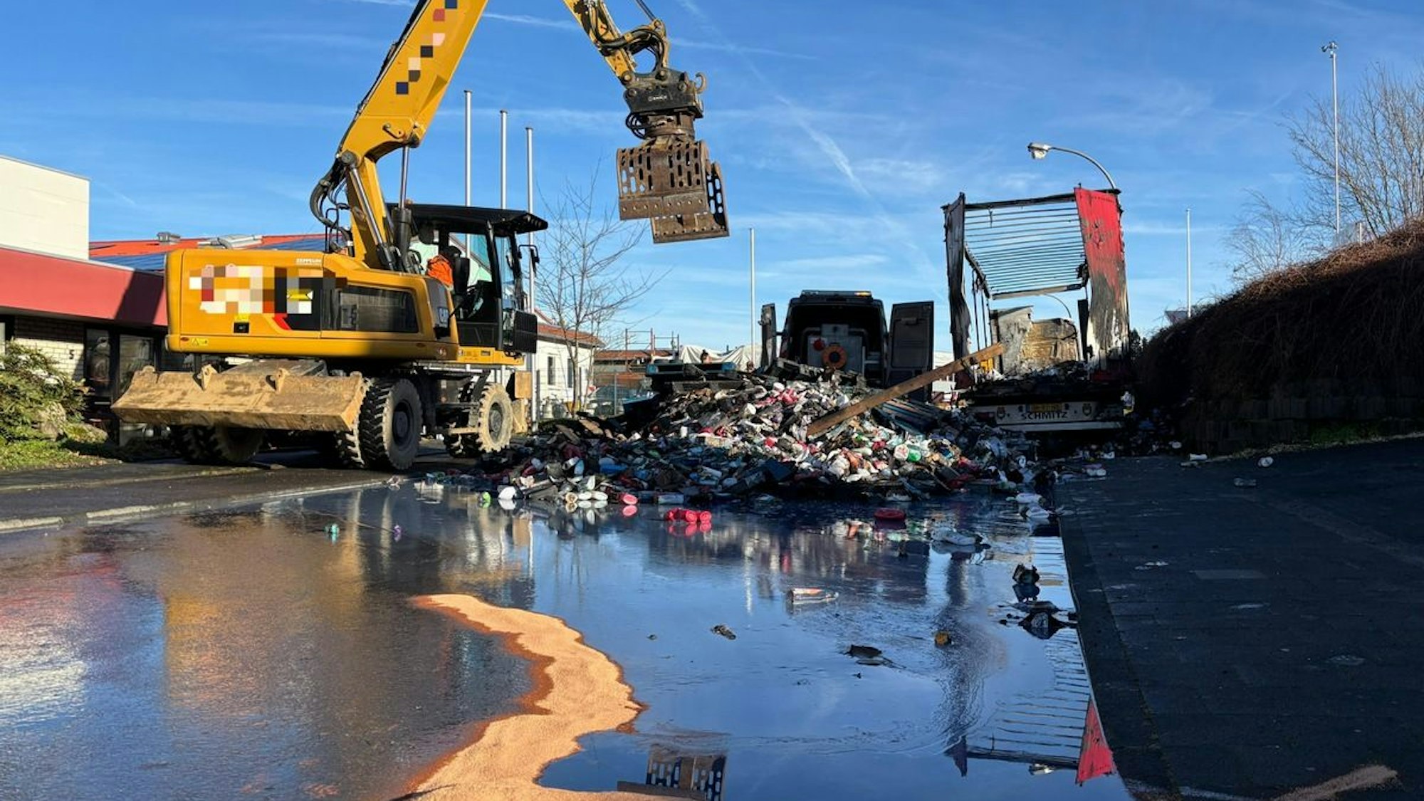 Ein ausgebrannter Lkw steht am Straßenrand, Feuerwehrleute sind im Hintergrund zu sehen.