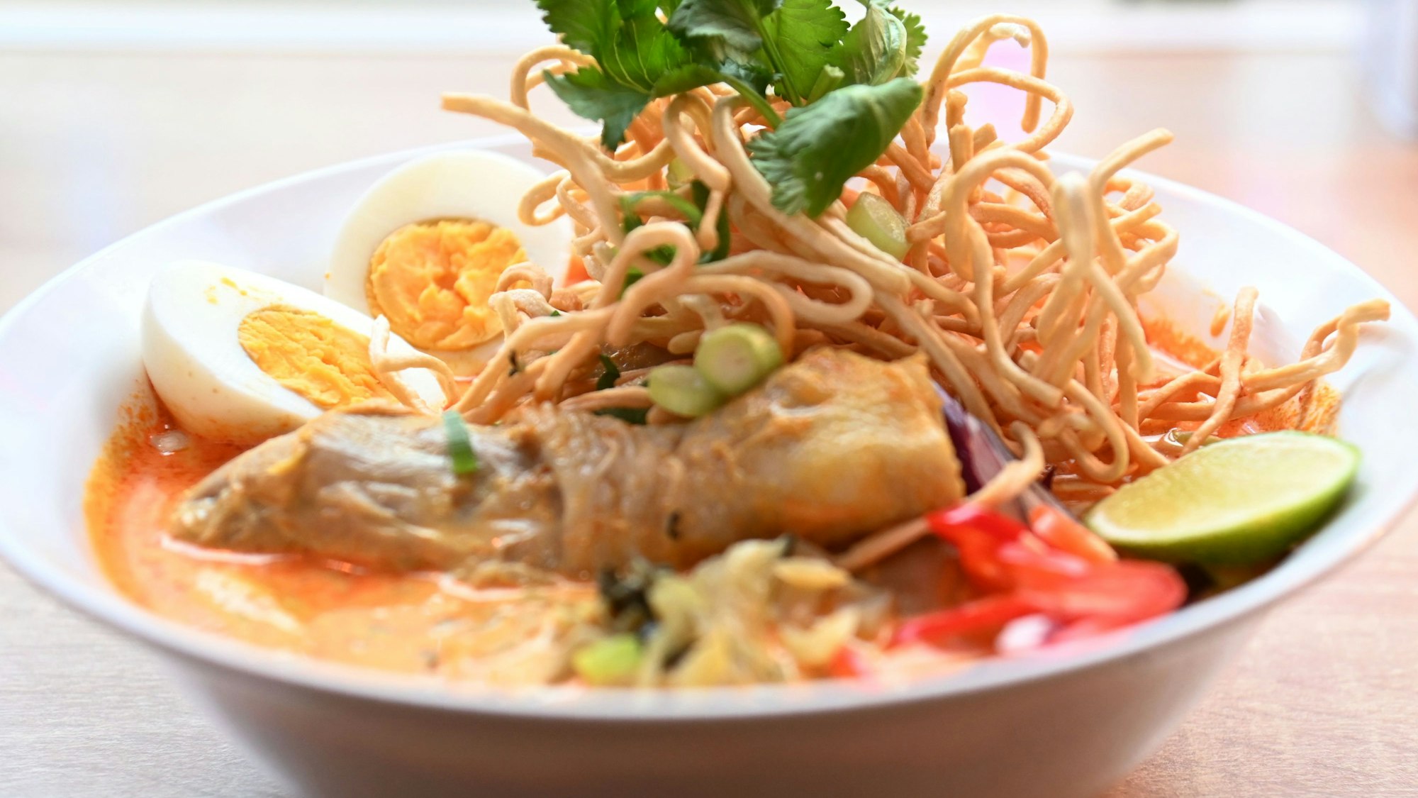 Khao Soi: Nudel-Curry-Suppe mit Hähnchenkeule und knusprigen Eiernudeln.