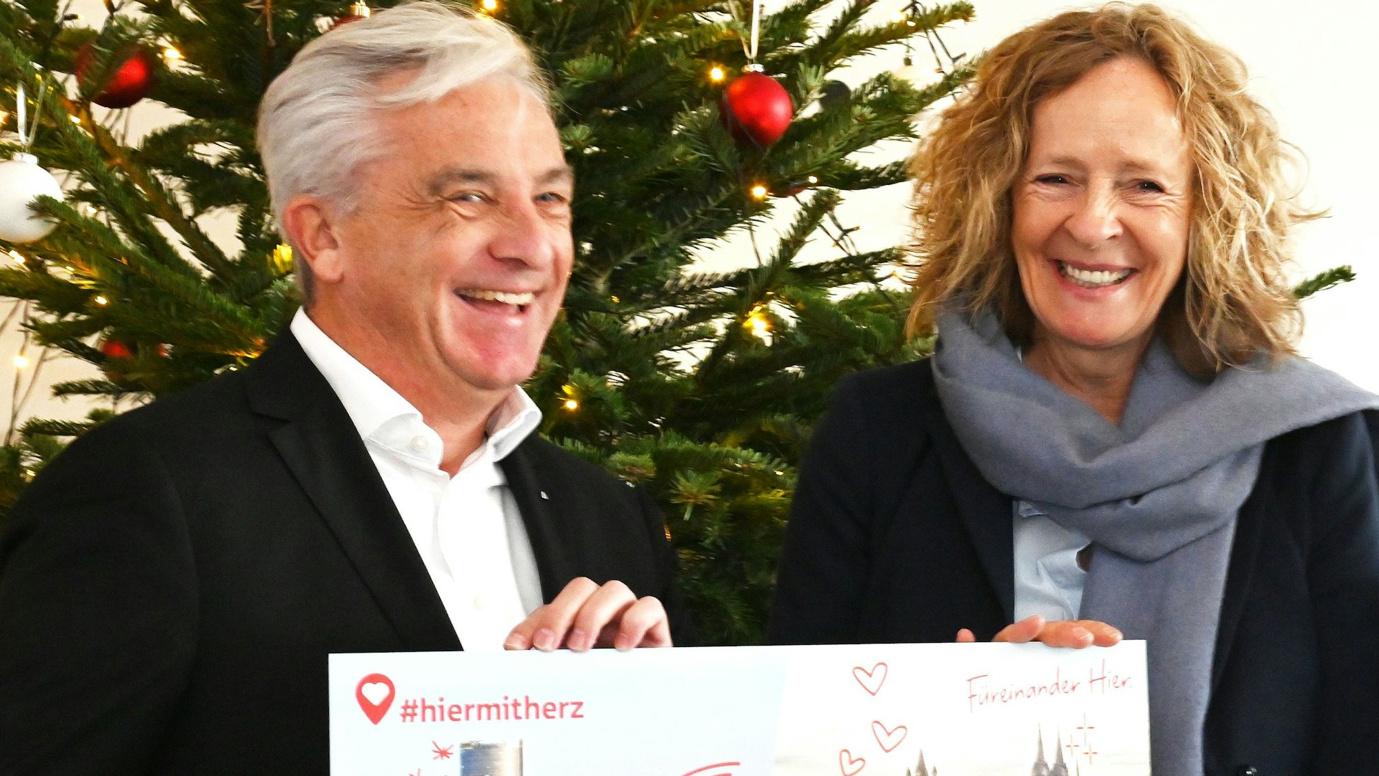 Rainer Virnich, Vorstandsmitglied der Sparkasse KölnBonn überreicht Herausgeberin Isabella Neven DuMont vor einem Weihnachtsbaum einen symbolischen Scheck für„ wir helfen e.V.“