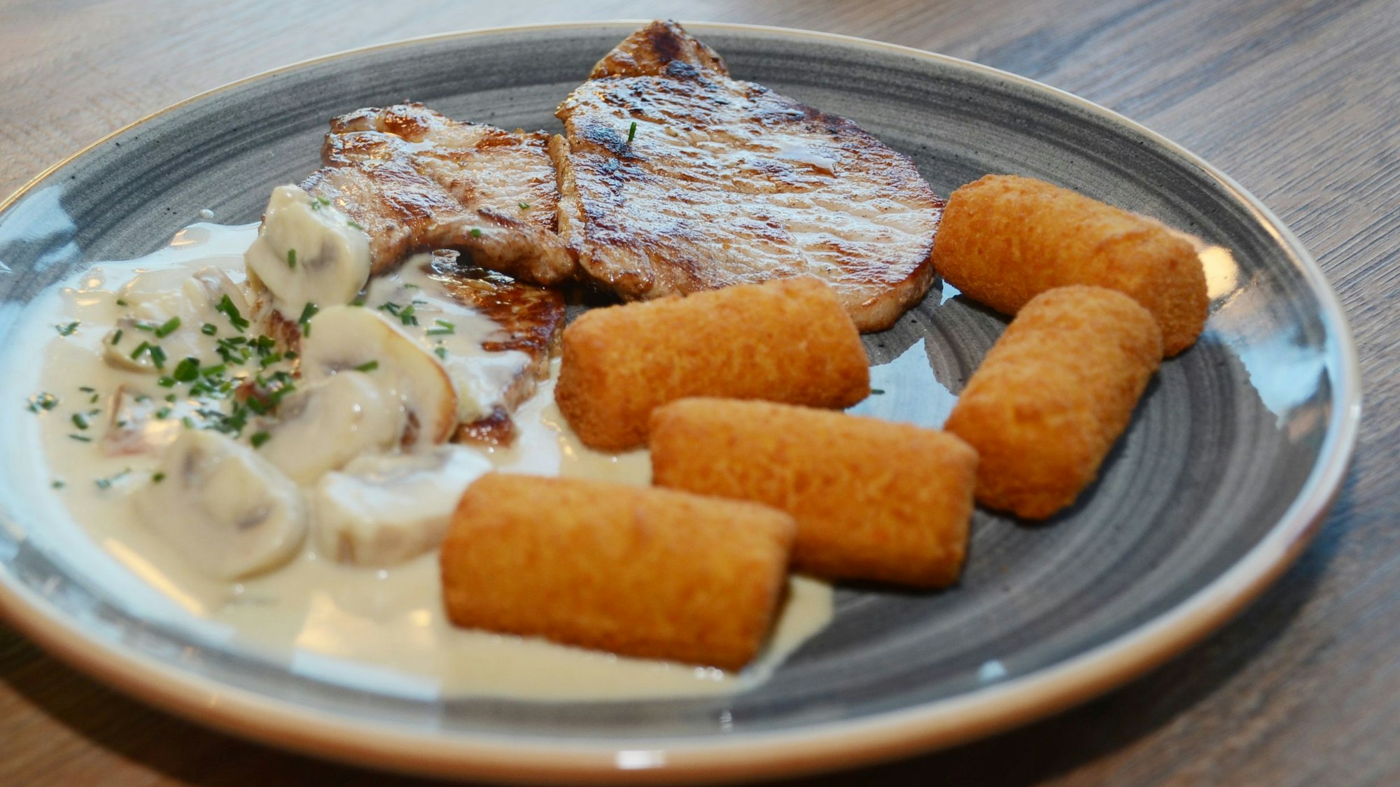 Schnitzel mit Pilzsauce und Kroketten auf einem Teller.