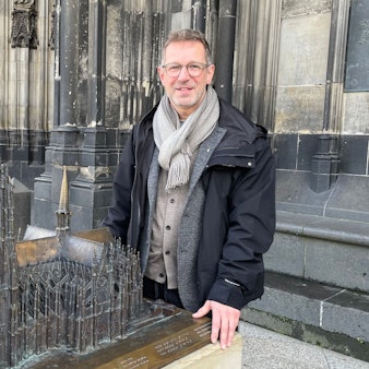 Ein Mann steht auf dem Vierungsturm des Kölner Doms, hinter ihm ragen die beiden Domtürme in den Himmel.