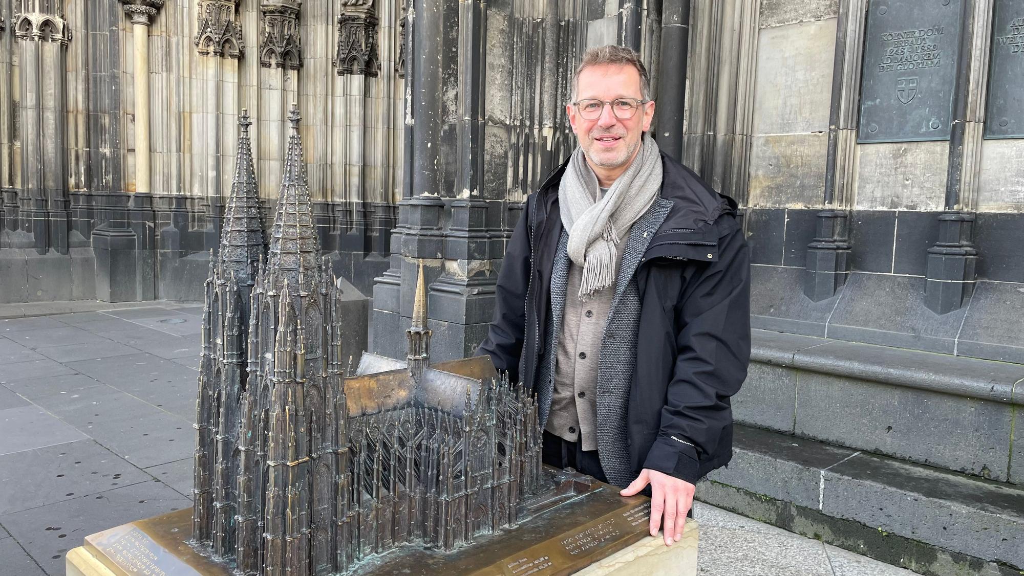 Ein Mann steht auf dem Vierungsturm des Kölner Doms, hinter ihm ragen die beiden Domtürme in den Himmel.
