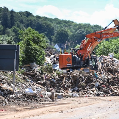 Das Bild zeigt einen Bagger, der Müll auf einen Lkw lädt. Auch ein Traktor samt Anhänger ist zu sehen.