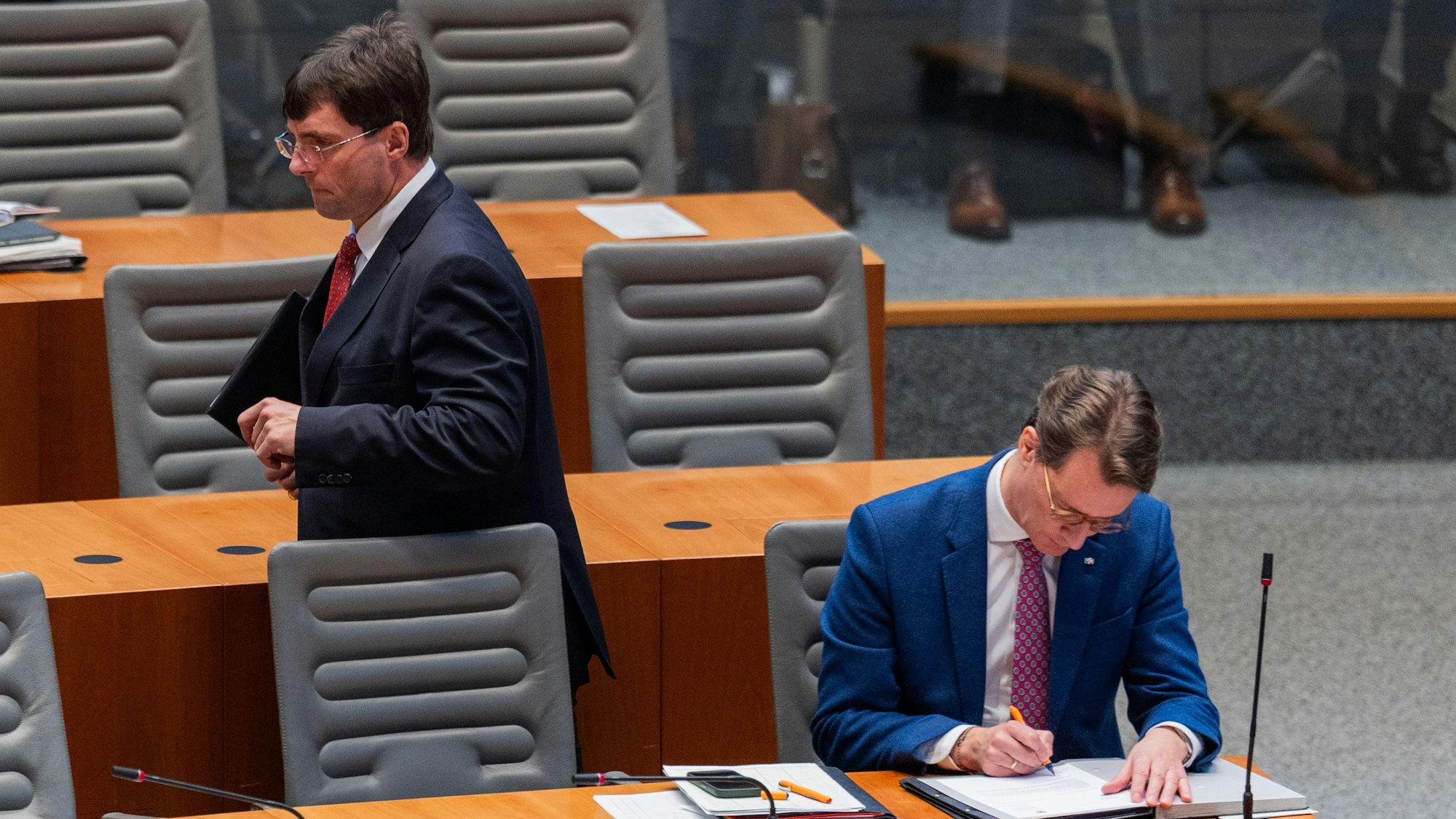 Marcus Optendrenk (l, CDU), Finanzminister von Nordrhein-Westfalen, geht an Hendrik Wüst (CDU), Ministerpräsident von Nordrhein-Westfalen, im Plenum des Landtags vorbei.