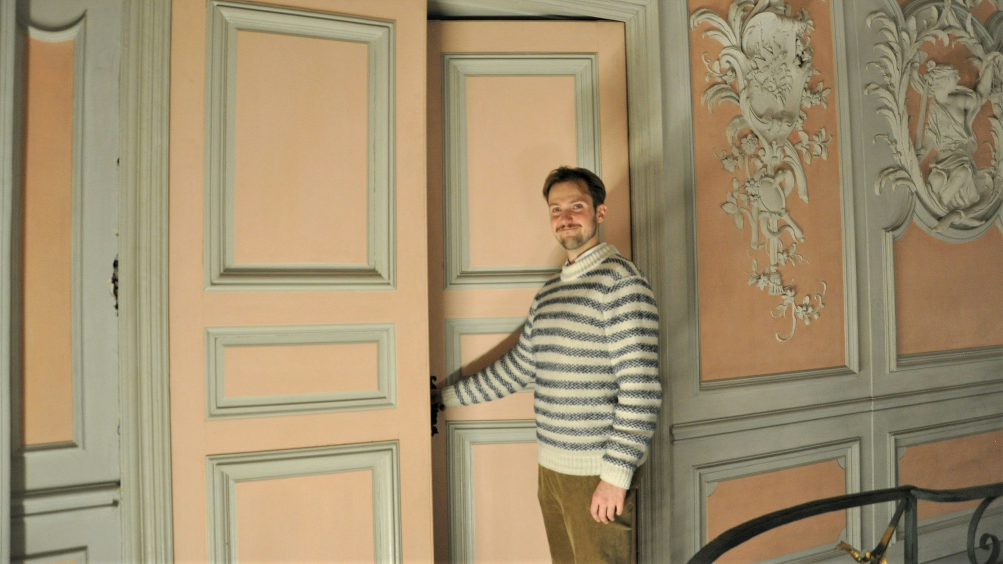 Auf dem Bild ist ein Mann im Pullover zu sehen, der eine Tür im Schloss Augustusburg öffnet.