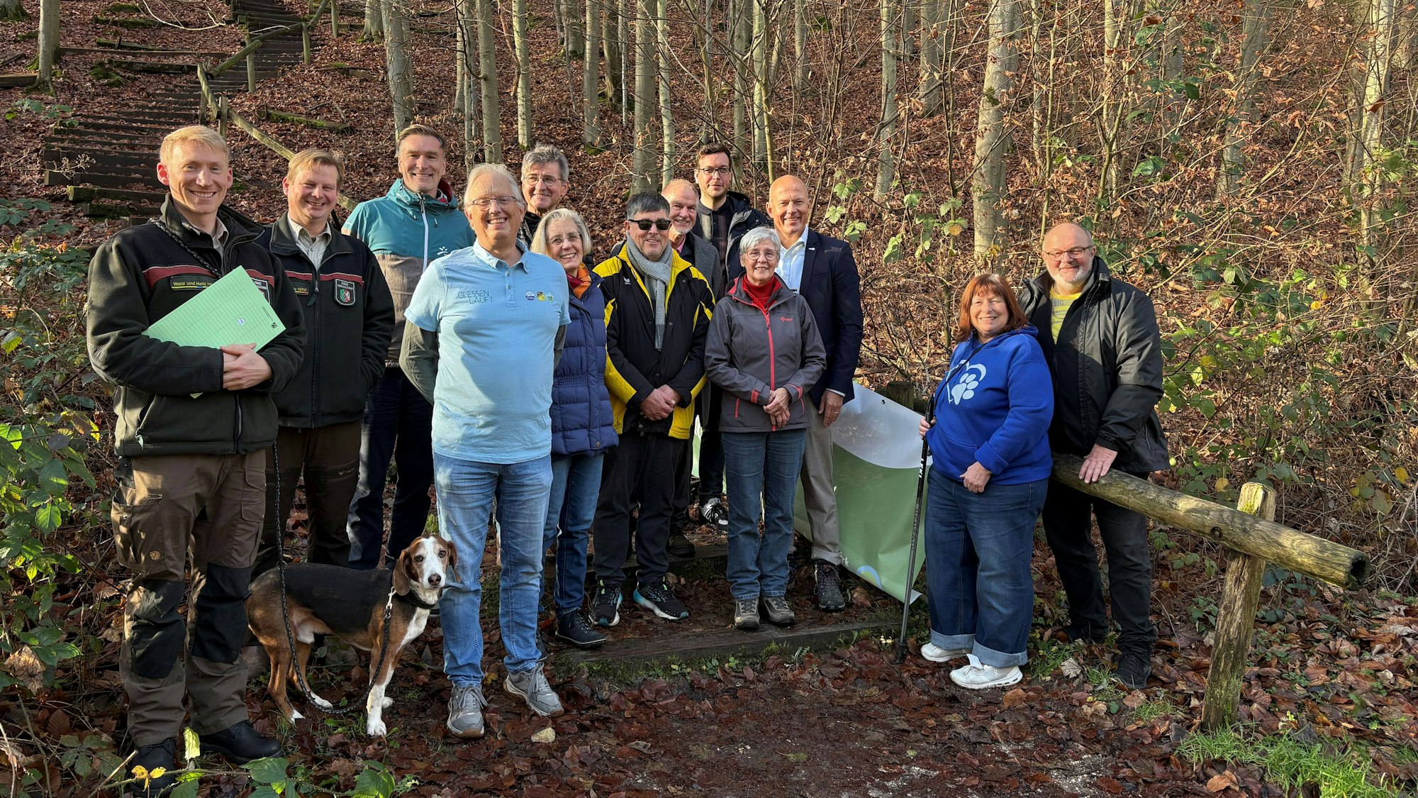 Auf dem Bild ist eine Gruppe von Männern und Frauen und ein Hund in einem Wald zu sehen.