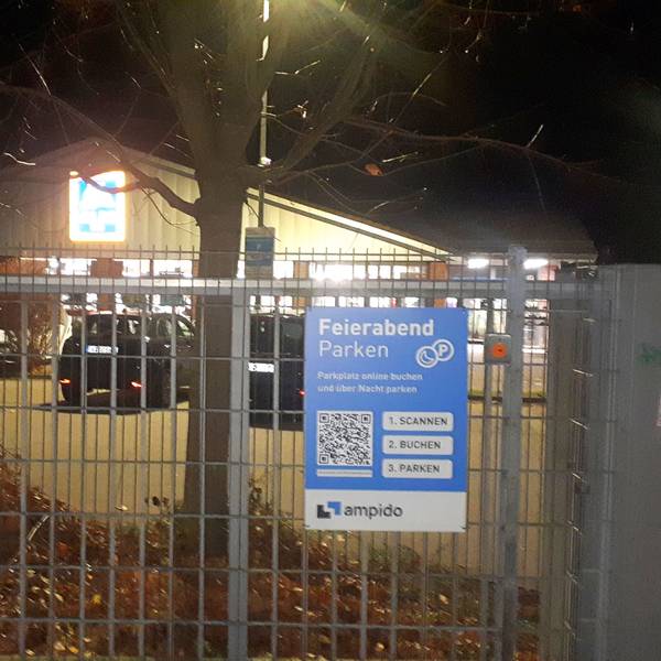 Hinter einem Gittertor stehen Autos auf einem Parkplatz