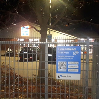 Hinter einem Gittertor stehen Autos auf einem Parkplatz