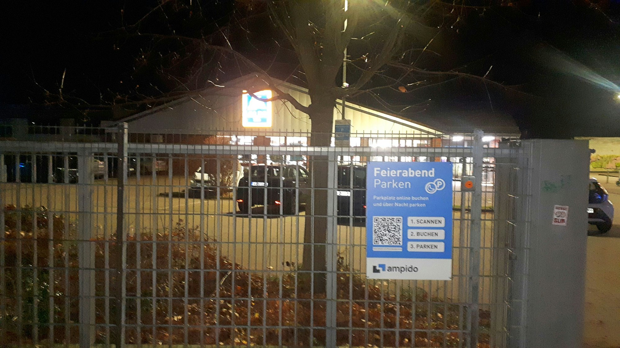 Hinter einem Gittertor stehen Autos auf einem Parkplatz