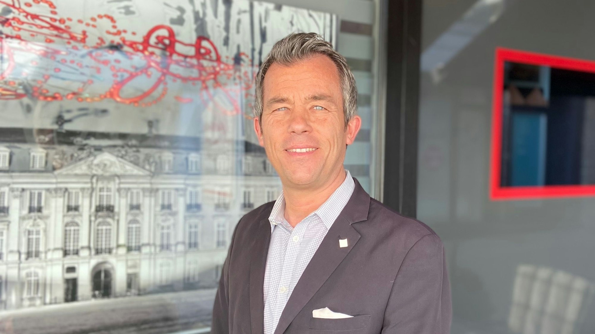 Auf dem Bild ist das Portrait eines Mannes im Sakko zu sehen.