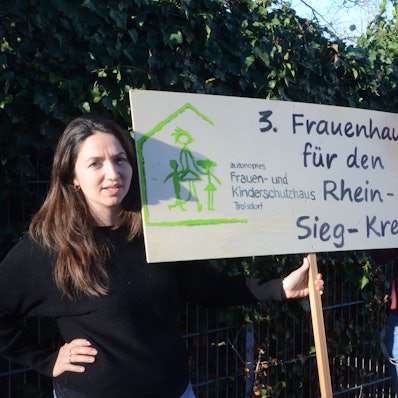 Zwei Frauen mit einem Schild. 3. Frauenhaus für den Rhein-Sieg-Kreis steht darauf.