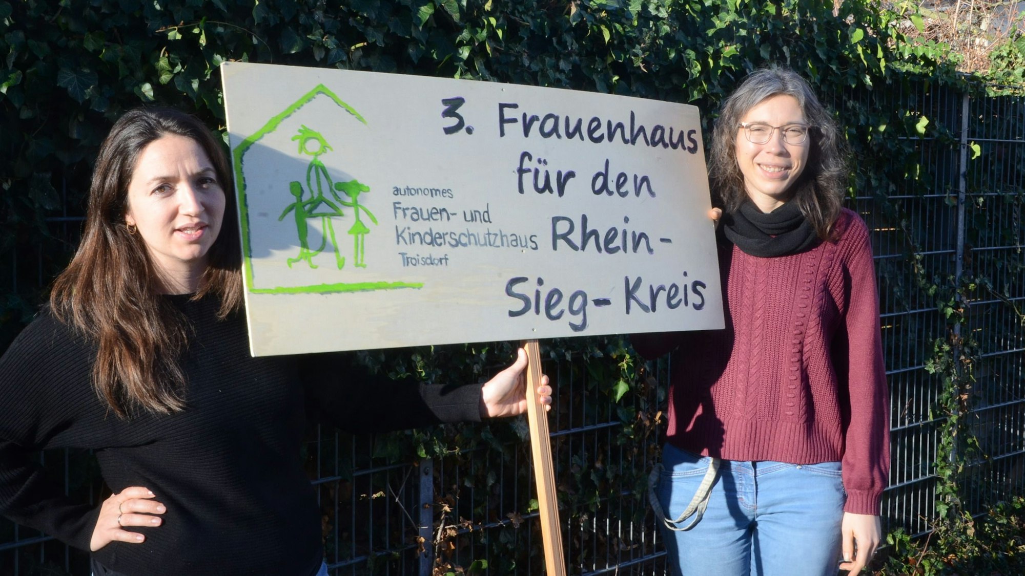 Zwei Frauen mit einem Schild. 3. Frauenhaus für den Rhein-Sieg-Kreis steht darauf.