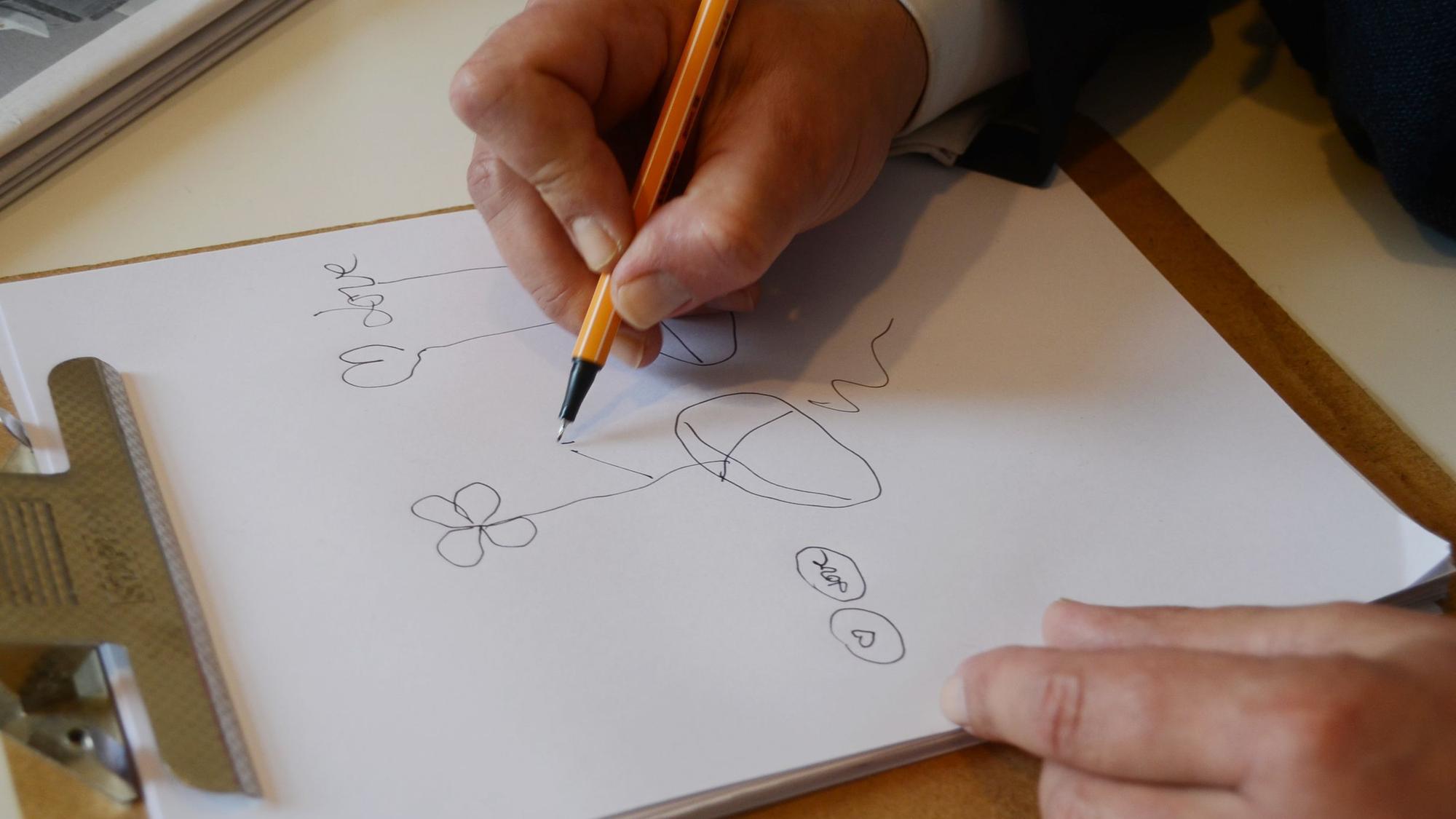 Eine Hand zeichnet mit Filzstift auf einem Blatt Papier.
