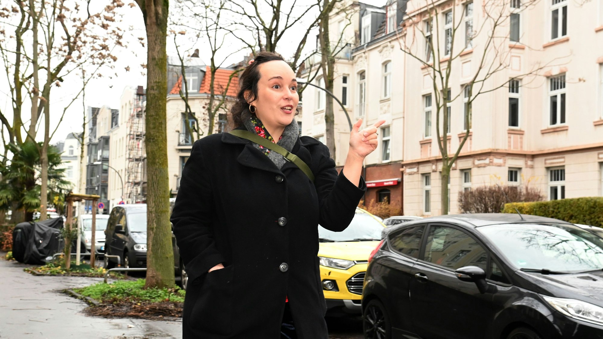 Eine Frau im dunklen Mantel läuft gestikulierend durch eine Straße.