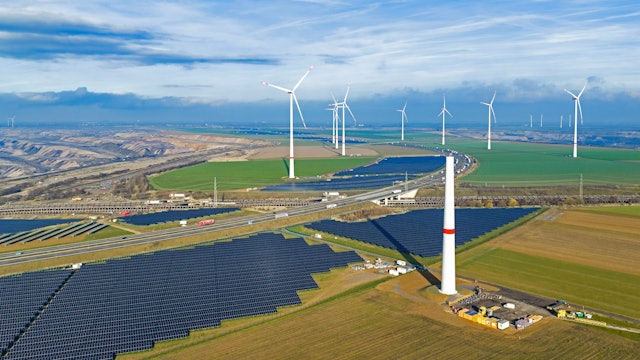 Zu sehen sind Solarmodule, fertige Windräder und im Vordergrund ein im Bau befindliches Windrad.