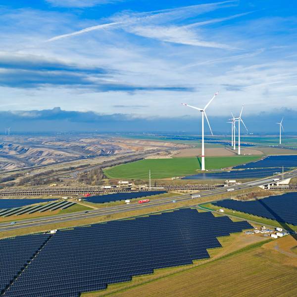Zu sehen sind Solarmodule, fertige Windräder und im Vordergrund ein im Bau befindliches Windrad.