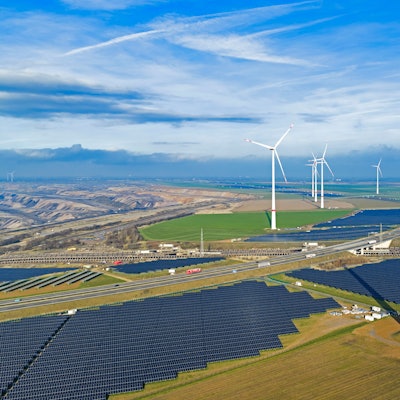 Zu sehen sind Solarmodule, fertige Windräder und im Vordergrund ein im Bau befindliches Windrad.