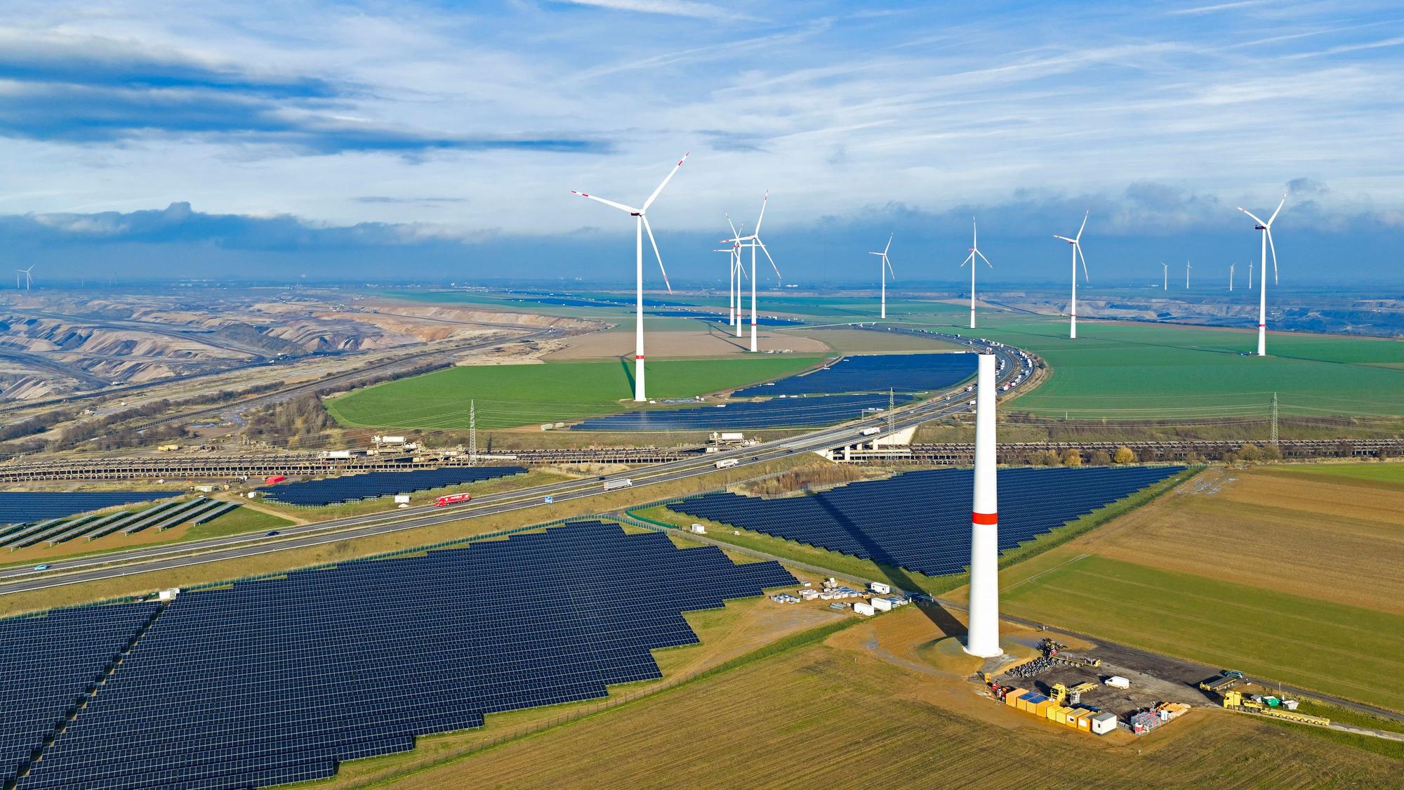 Zu sehen sind Solarmodule, fertige Windräder und im Vordergrund ein im Bau befindliches Windrad.