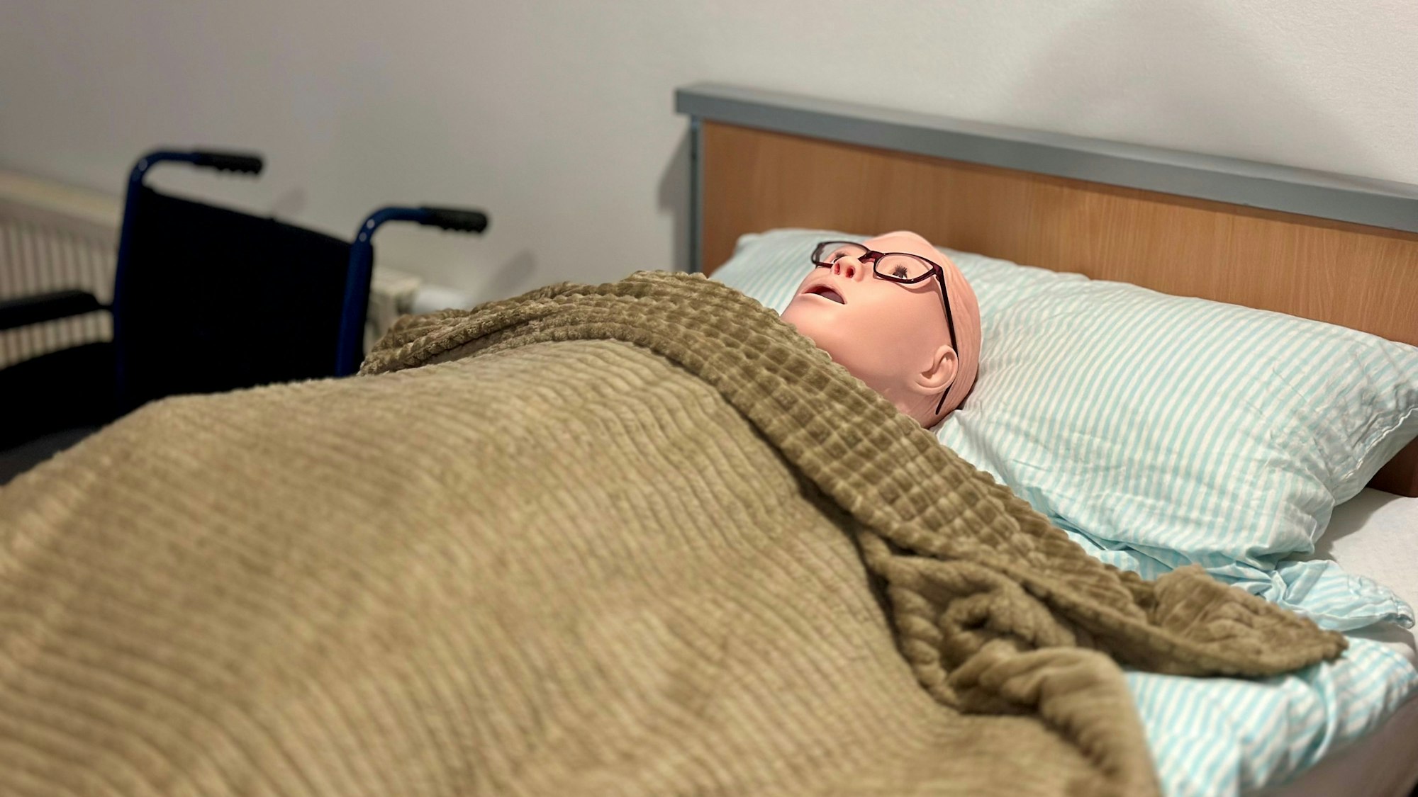 Eine Puppe liegt unter einer Decke in einem Bett.