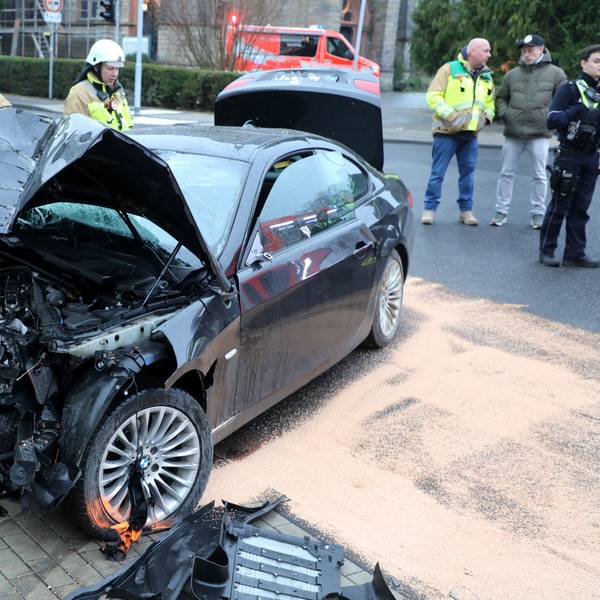 Ein total demoliertes Fahrzeug steht auf der Straße, Feuerwehrleute schauen darauf, haben ausgelaufene Betriebsstoffe und Öl abgestreut.