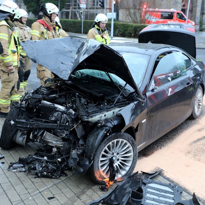 Ein total demoliertes Fahrzeug steht auf der Straße, Feuerwehrleute schauen darauf, haben ausgelaufene Betriebsstoffe und Öl abgestreut.