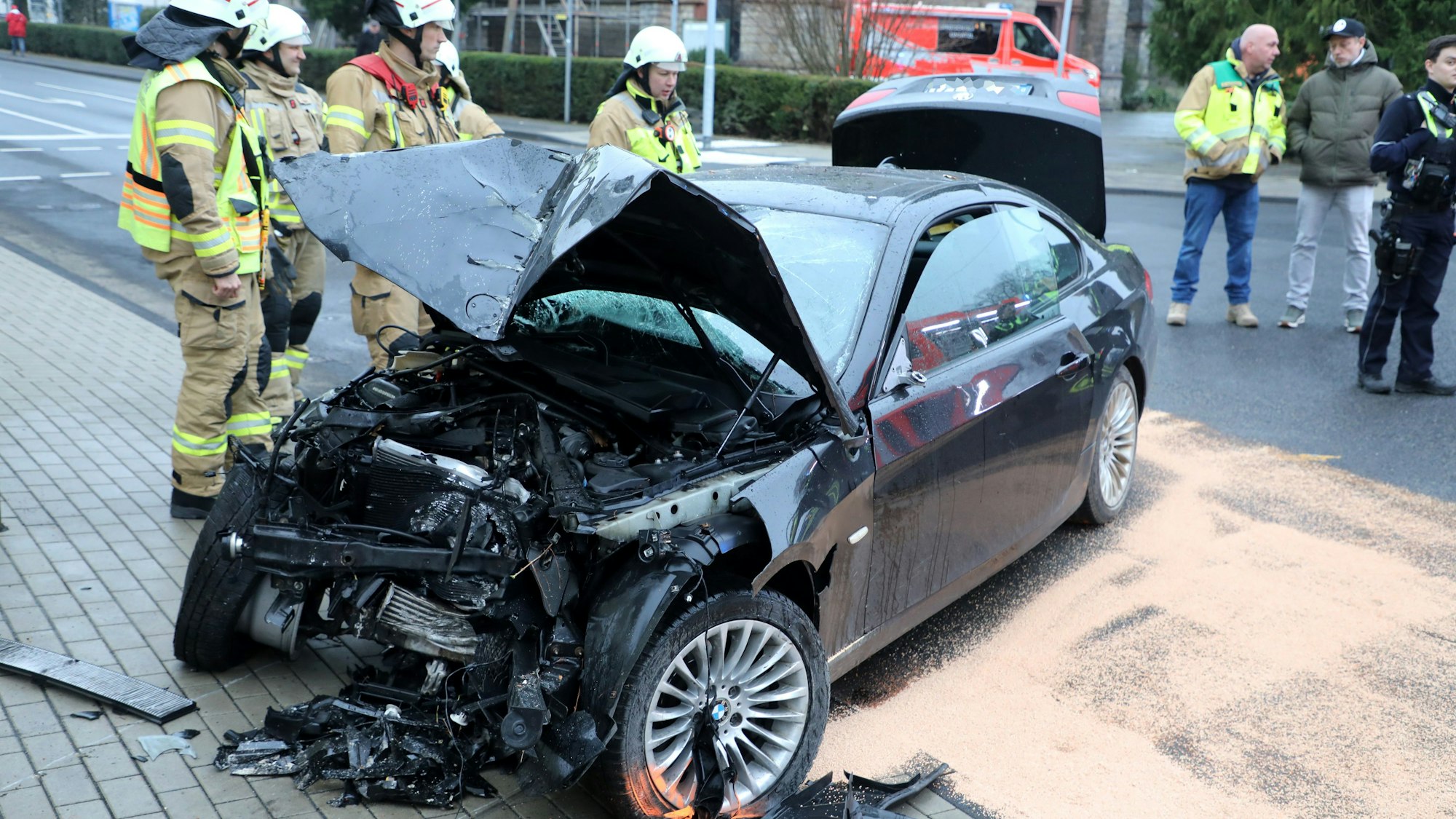 Ein total demoliertes Fahrzeug steht auf der Straße, Feuerwehrleute schauen darauf, haben ausgelaufene Betriebsstoffe und Öl abgestreut.