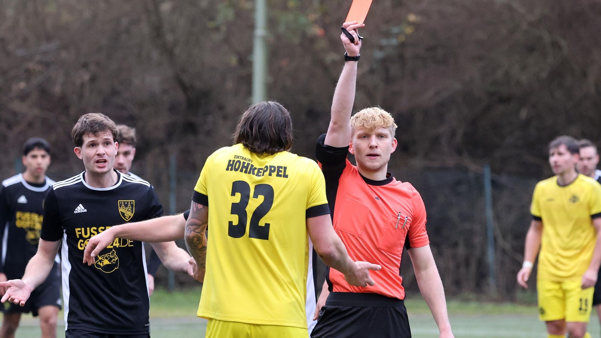 Ein Schiedsrichter zeigt einem Fußballer die gelb-rote Karte.