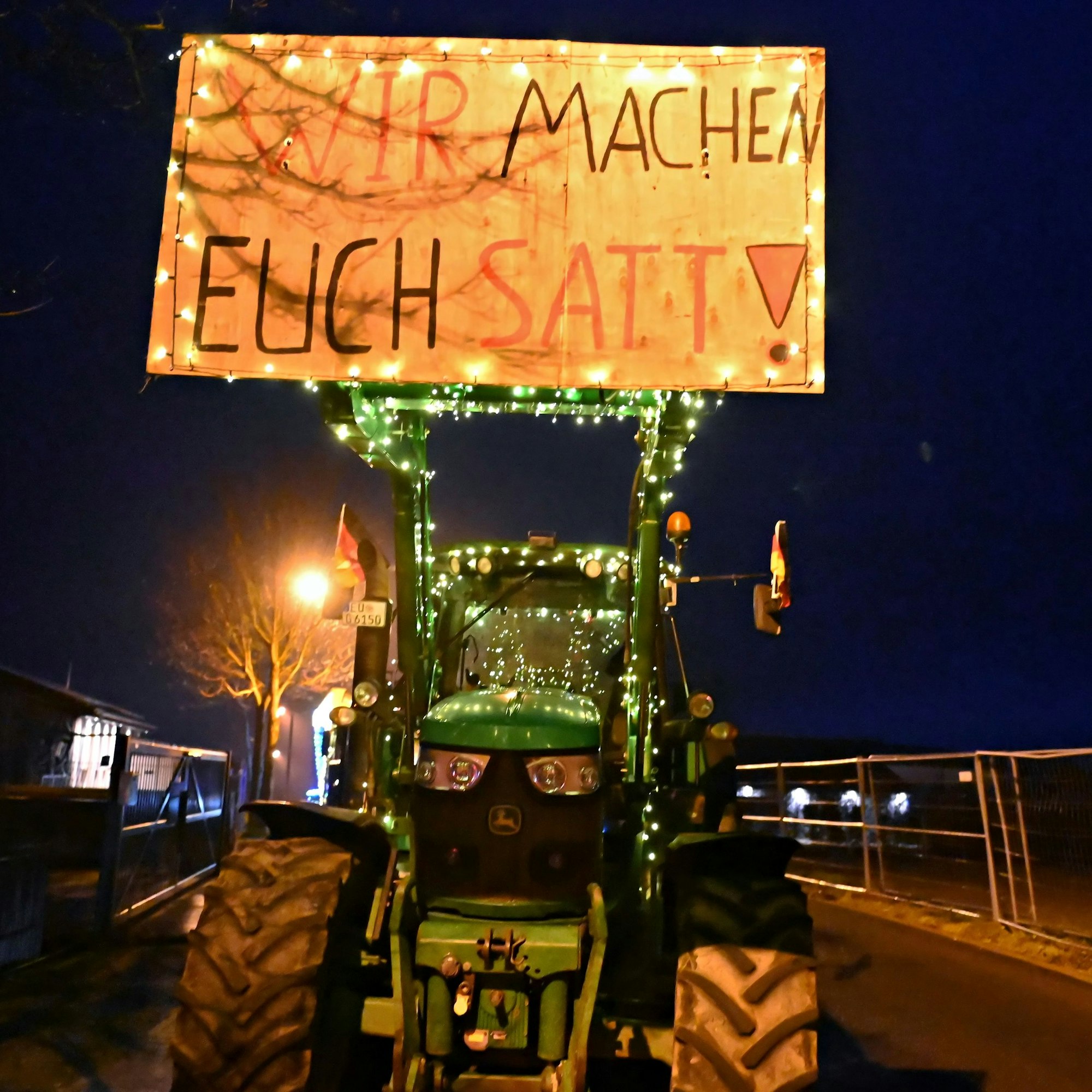 Ein Traktor hat das Plakat mit der Aufschrift „Wir machen Euch satt!“ am Frontlader befestigt.