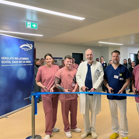 Eine Frau und vier Männer durchschneiden ein blaues Band, hinter dem sie in einer Reihe stehen.